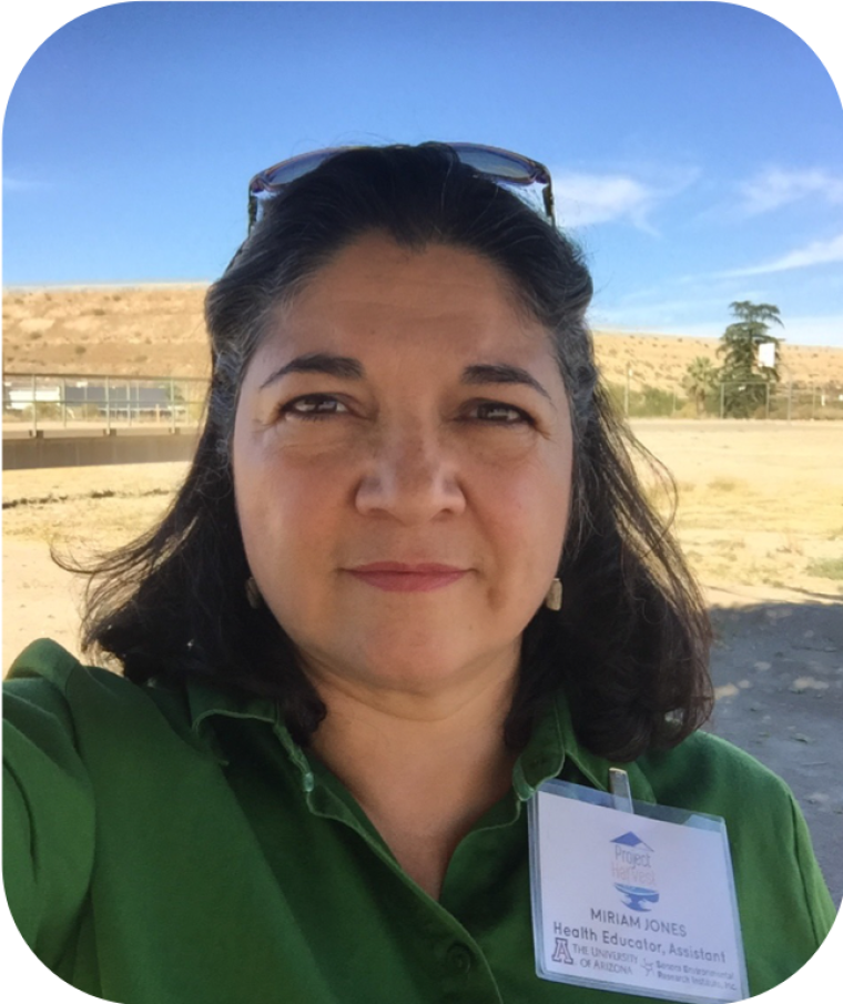 Photo of a person in a green blouse with a printed Project Harvest nametag in front of a field and a fence line in background